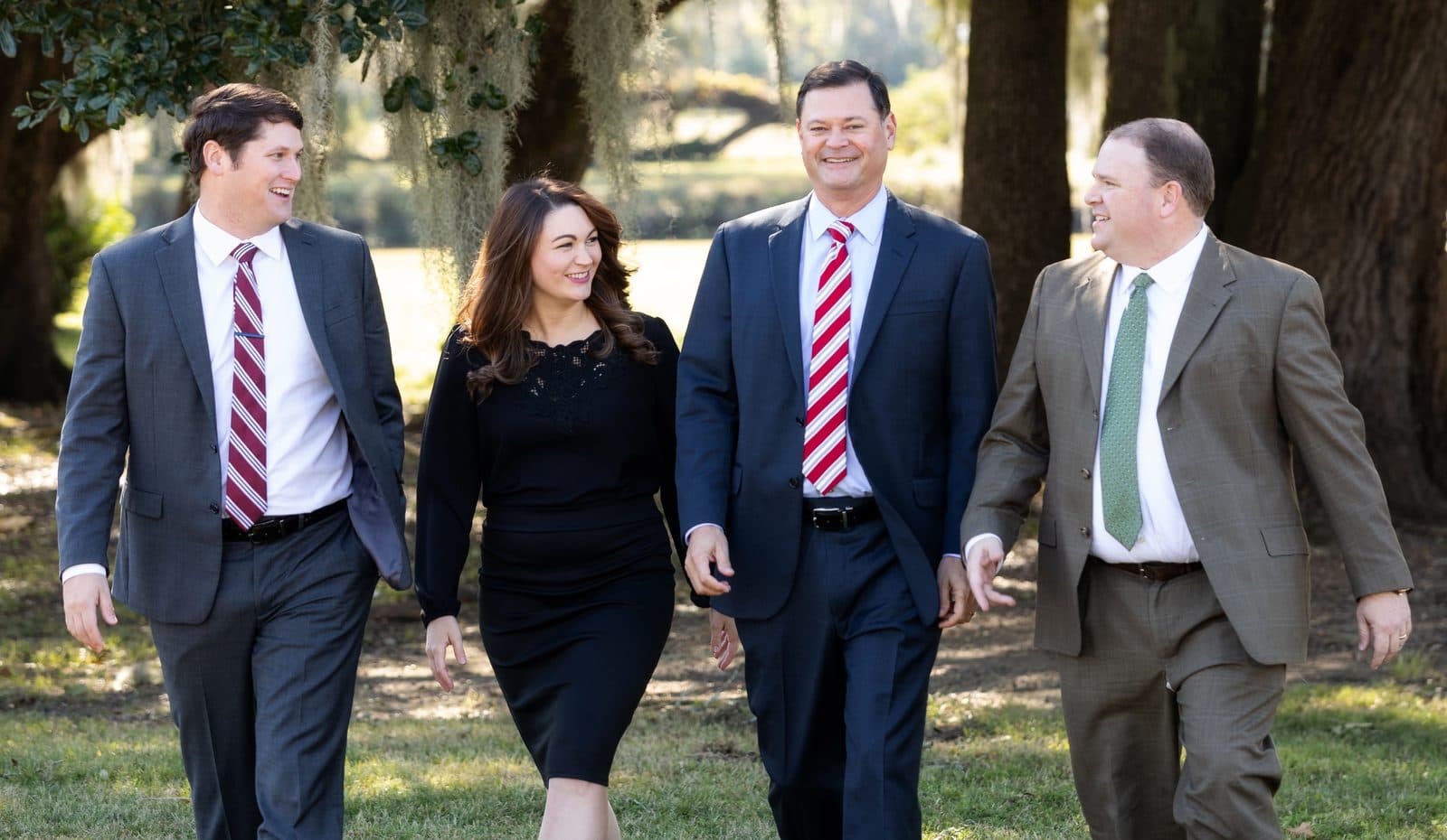 The four attorneys of The Tadda Law Firm walking together outdoors beneath live oaks